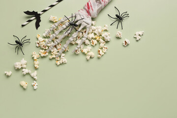 Composition with tasty popcorn, skeleton hand, spiders and straw for Halloween celebration on green background