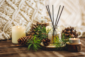 Natural aromatic scented reed diffuser air freshener bottle on wooden table with pine cone, burning...