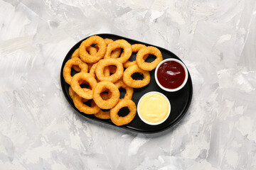 Plate with fried breaded onion rings and different sauces on grey background