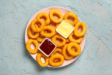 Plate with fried breaded onion rings and different sauces on blue background