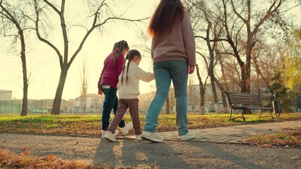 Happy family walk in the park in autumn. Mothers and children, daughters walk in the park, holding hands. Happy healthy family concept. Mother and children walk together outdoors. Family weekend