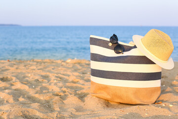 Stylish black sunglasses with bag and hat on seashore