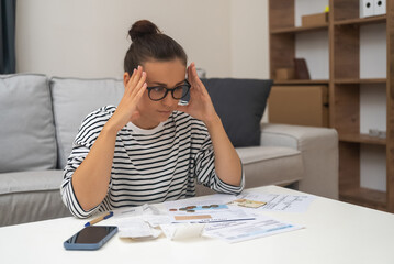 Budget Distress: Stressed by debt, a woman manages household finances, calculates expenses, and seeks solace in online payments while feeling unhappy.