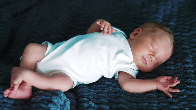 Lovely tiny baby boy in white bodysuit. Adorable newborn sleeping tight on the blue blanket.