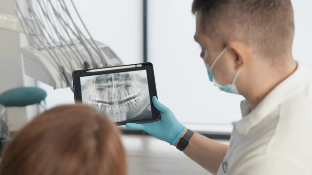 The dentist shows the results of panoramic tomography of the patient's teeth on a tablet. The patient receives an examination, consultation and treatment plan for her oral cavity using an X-ray