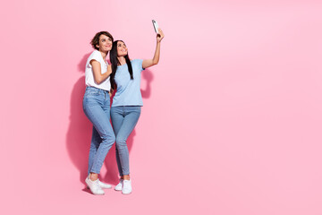 Full body length cadre of two friendly charming girls sisters spend free time shopping mall selfie camera isolated on pink color background