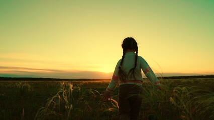 Happy child runs with arms raised like airplane wings, childhood dream in park. Child aviator runs across field, kid dreams of becoming an airplane pilot. Silhouette of child girl running at sunset.
