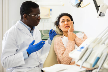 Asian woman complaining about toothache to african-american man dentist during consulatation in...