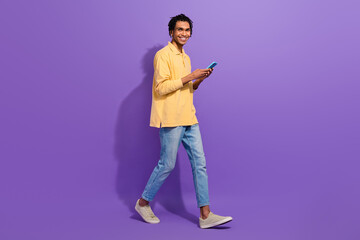 Full length photo of funky guy walking with apple smartphone texting social medias network connection isolated on violet color background