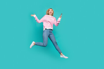 Full length photo of cute excited girl dressed striped sweater typing apple samsung iphone gadget isolated teal color background