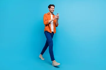 Zelfklevend Fotobehang Full length profile photo of cheerful nice man hold use smart phone texting typing post isolated on blue color background © deagreez