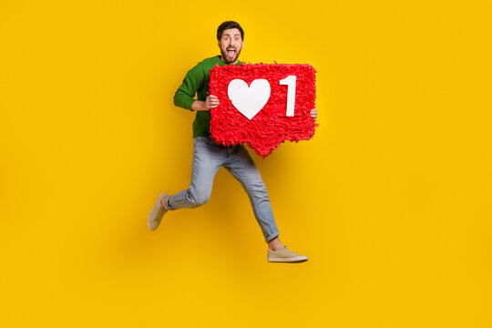 Full length photo of crazy young man brunet jump hold pinata notification red heart click like symbol isolated on yellow color background