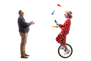 Full length profile shot of a mature man giving an applause to a clown riding a unicycle and juggling