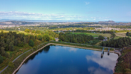 Scottish countryside - Reservoir Torduff and Edinburgh view from the sky. A small elongated reservoir retained by an earth embankment dam in the City of Edinburgh.