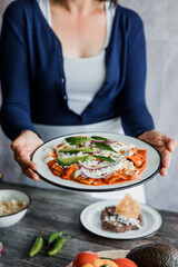 Mexican woman hands preparing chilaquiles with red sauce and eating traditional mexican food for breakfast in Mexico Latin America