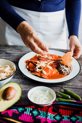 Mexican woman hands preparing chilaquiles with red sauce and eating traditional mexican food for breakfast in Mexico Latin America