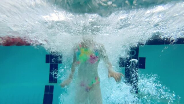 Happy child dives into the pool from the diving tower. A teenage girl in a bright swimsuit swiming in the pool