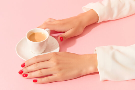 Womans hands with red manicure holding cup on pink background. Minimalist nail design.