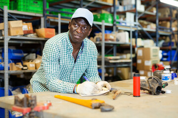 Portrait of focused African-American man worker checking order list at workplace in warehouse of hardware store
