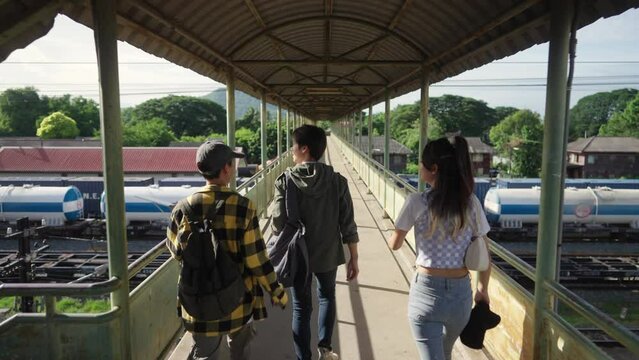 4K Group of Diversity Asian man and woman friends enjoy and fun outdoor lifestyle walking together on crossing bridge at train station during travel local town in Thailand on summer holiday vacation.