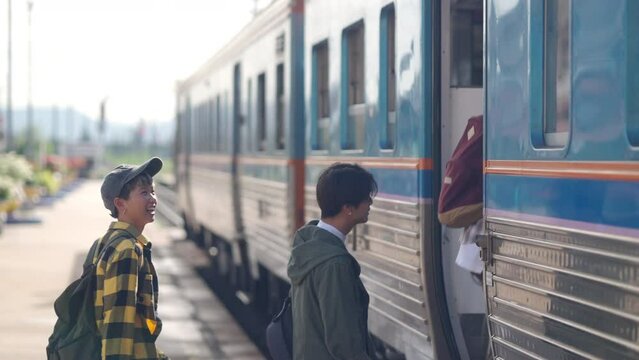 Group of Young Asian people get on the train at local railway station. Man and woman friends enjoy and fun outdoor lifestyle travel in Thailand by public transportation on summer holiday vacation.