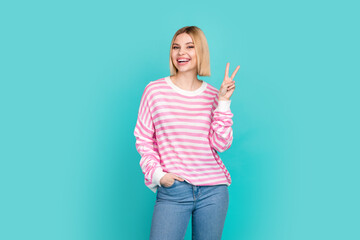 Photo of excited funky girl dressed striped sweater smiling showing v-sign isolated teal color...