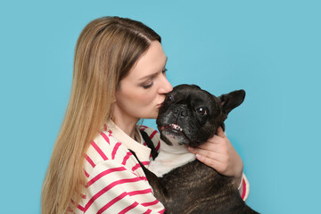 Woman hugging cute French Bulldog on light blue background