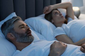 Irritated woman lying near her snoring husband in bed at home