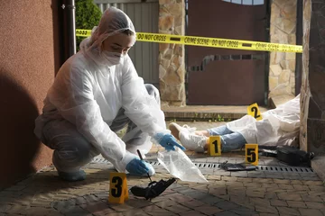 Gordijnen Criminologist in protective gloves working at crime scene with dead body outdoors © New Africa