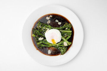 Tasty cooked broccolini with poached egg, almonds and sauce on white background, top view
