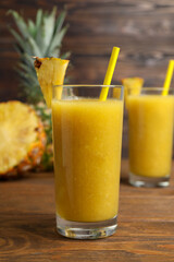 Tasty pineapple smoothie, whole and cut fruit on wooden table
