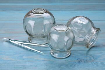 Glass cups and tweezers on light blue wooden table, closeup. Cupping therapy