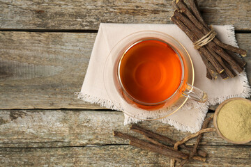 Aromatic licorice tea in cup, dried sticks of licorice root and powder on wooden table, flat lay. Space for text