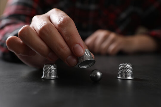 Woman playing thimblerig game with thimbles and metal ball at black table, closeup