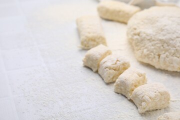 Fototapeta na wymiar Making lazy dumplings. Raw dough and flour on white tiled table, closeup. Space for text