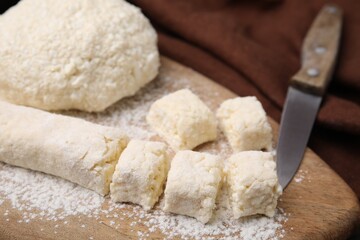 Making lazy dumplings. Raw dough, flour and knife on wooden board, closeup