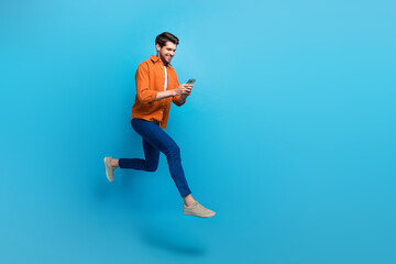 Fototapeta na wymiar Full size profile photo of energetic attractive man use smart phone jumping run hurry empty space ad isolated on blue color background