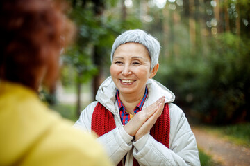 Cheerful pensioner female friends tallking and laughing in the autumn park.