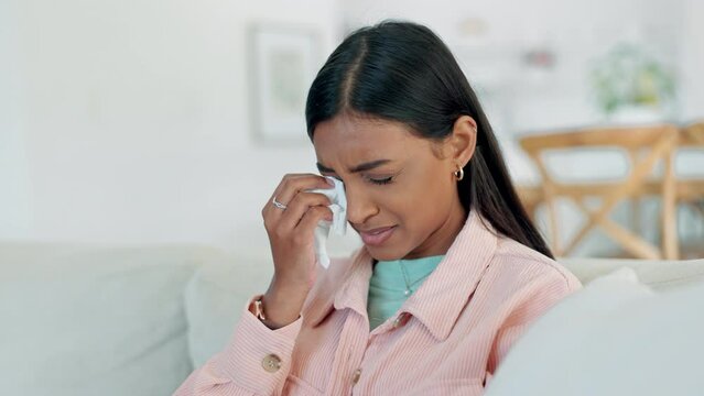 Woman, depression and crying on sofa for sad news, mental health or psychology at home. Indian person, tissue and wipe tears for trauma, anxiety and pain of broken heart, divorce or grief counselling