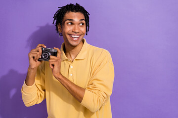 Photo of young funky guy dreadlock hair holding old school vintage camera looking empty space shooting isolated on purple color background