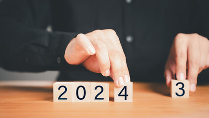 Male hand holding a wooden cube block with numbers 2024 on wood table. Goal in the new year 2024. Business development strategy, advancement and goal concept.