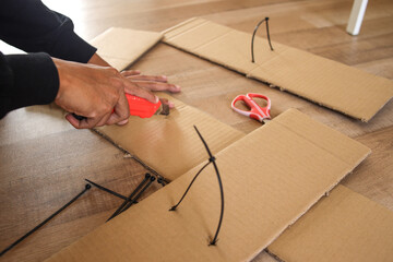 Obraz na płótnie Canvas Male hand cutting cardboard box with cutter at home making kid toys