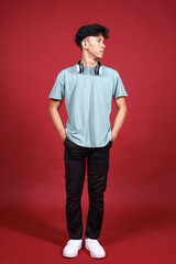 Fototapeta premium Full length of smiling young Asian man wearing headphones looking aside isolated on crimson red background