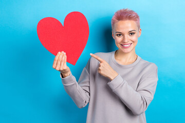Portrait of charming cheerful lady toothy smile indicate finger empty space heart symbol card isolated on blue color background
