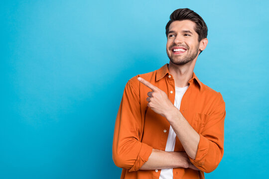 Photo of attractive dreamy man dressed orange shirt looking showing finger empty space isolated blue color background