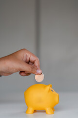 Close up woman puts coins in a piggy bank with a pile of coins to save money.