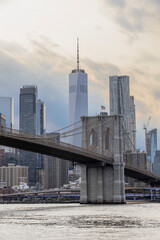 Fototapeta premium The iconic Brooklyn Bridge crosses the East River leading into Manhattan, with sun beams shining down on New York City's skyscrapers.