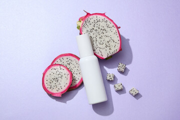 A white cosmetic bottle displayed on a purple background with fresh dragon fruit slices. Dragon fruit extract is often used to make serums and skin-brightening creams. Minimal concept for advertising