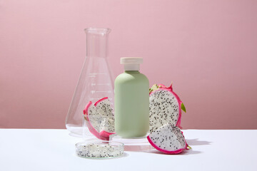 Front view of fresh dragon fruit slices decorated with green bottle mockup and lab glassware on a pink background. Scene for advertising cosmetic of natural extract. Cosmetics bottle for design