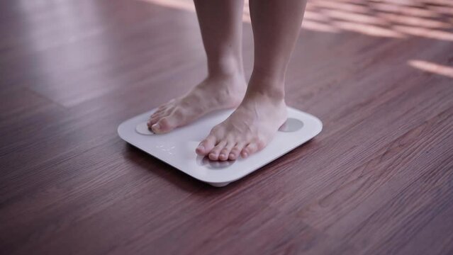 Healthy and weight loss concept, Young Asian woman stepping on weighing scales after weight control